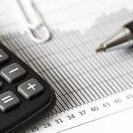 Kalkulator finansowy leżący obok wykresu i dokumentów z długopisem