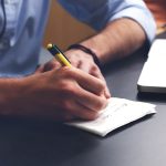Mężczyzna notujący pomysły biznesowe w notesie przy laptopie